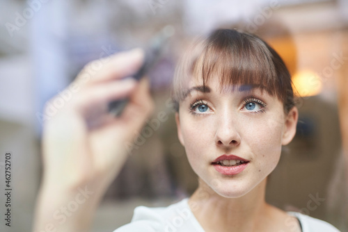 Portrait of young businesswoman writing on glass pane