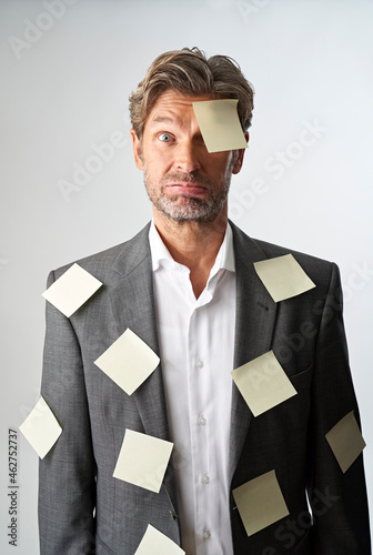 Portrait of helpless businessman with note papers stucking on his forehead and his suit coat