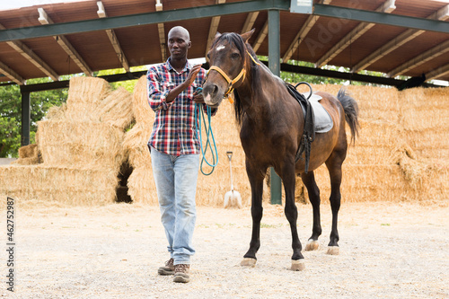 Young man farmer standing with horse at stable at farm outdoor