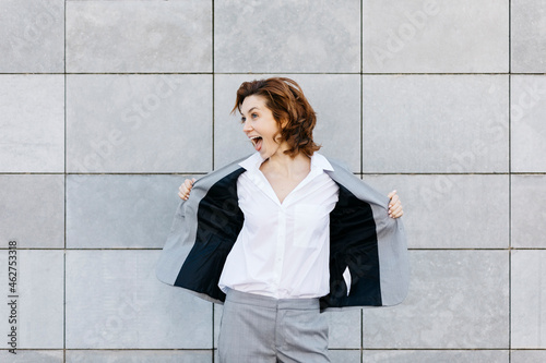 Portrait of a screaming young businesswoman in front of wall with gray tiles, opening her jacket
