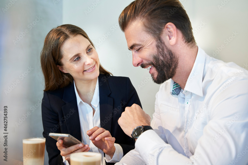 Businesswoman sharing cell phone with happy businessman in a cafe Businesswoman sharing cell phone with happy businessman in a cafe