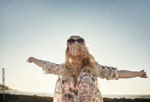 Carefree young woman covering face with hair while dancing at beach against clear sky photo