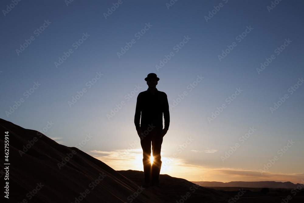 Morocco, Merzouga, Erg Chebbi, silhouette of man wearing a bowler hat standing on desert dune at sunset