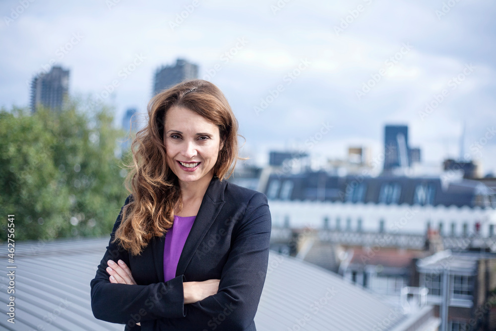 Confident smiling female entrepreneur standing with arms crossed at terrace against sky Confident smiling female entrepreneur standing with arms crossed at terrace against sky