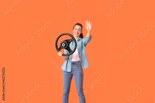 Young woman with steering wheel waving hand on color background © Pixel-Shot