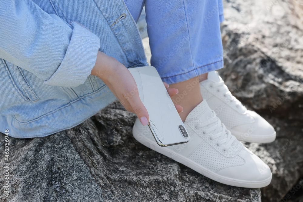Woman picking damaged mobile phone from stone outdoors, closeup