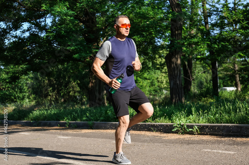 Sporty mature man with bottle of water running in park © Pixel-Shot