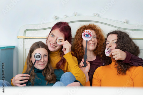 Family portrait of mother and her three daughters sitting together on bed holding paper masks