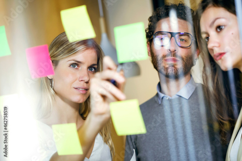 Three business people brainstorming together with sticky notes on a glass wall