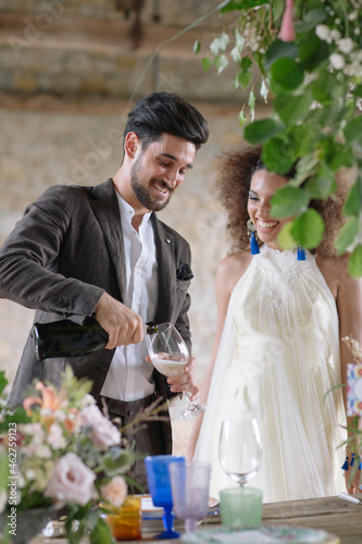 Smiling groom pouring champagne in flute while standing at table
