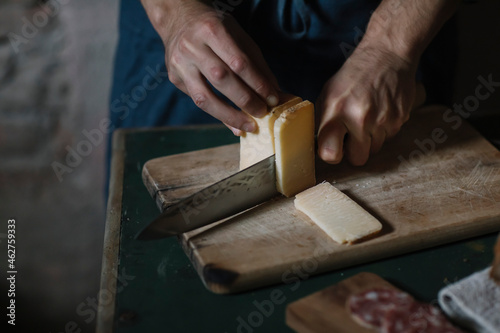 Hands of man cutting artisanal cheese slices on board at table photo