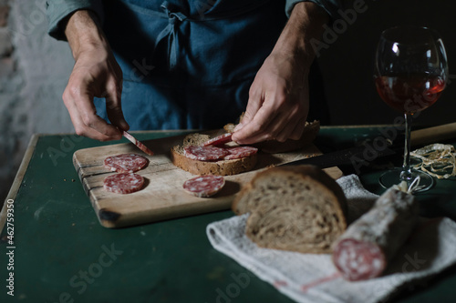 Midsection of young man preparing salami sandwich on cutting board at table photo