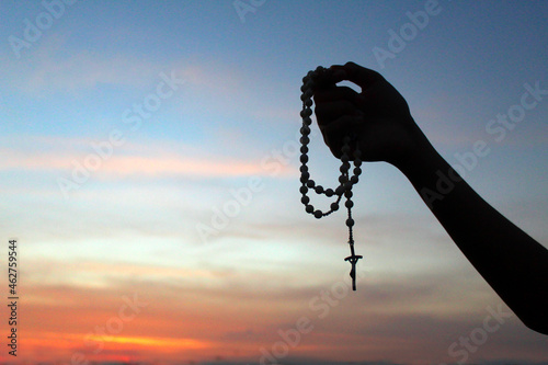 Silhouette of a hand holding Rosary on colorful sunset sky background. Person with Rosary in hands with Jesus Christ holy cross crucifix. Copy space for spiritual text message design. Catholic symbol. photo