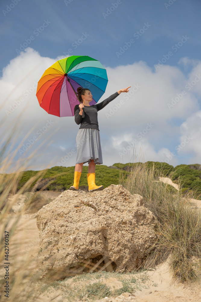 Woman with colorful umbrella standing on a rock and looking at distance Woman with colorful umbrella standing on a rock and looking at distance