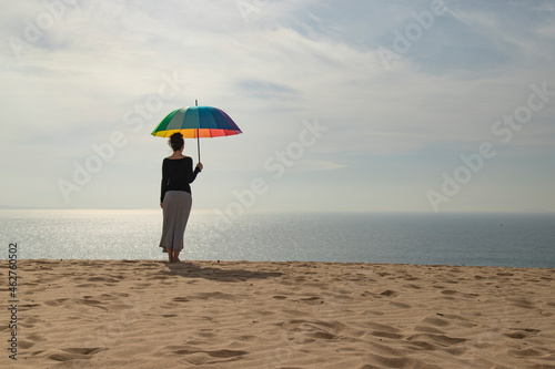 Woman with colorful umbrella standing at the beach, rear view photo