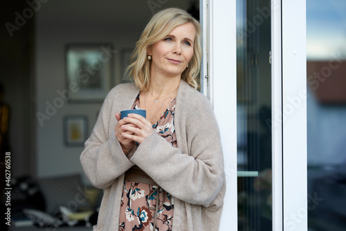 Blond woman leaning against balcony door at home