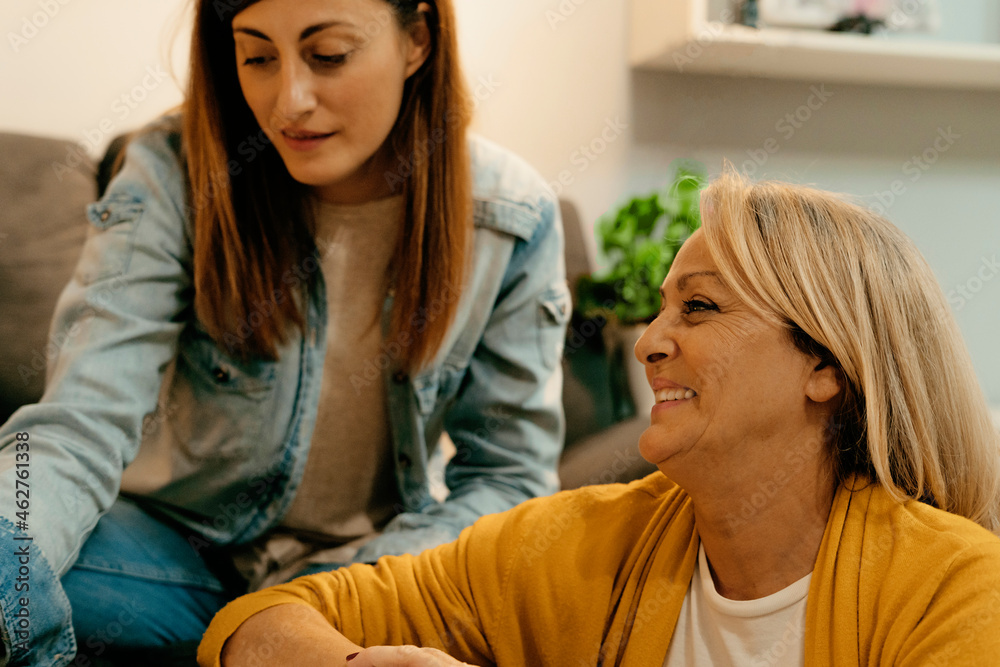Smiling senior mother sitting besides daughter at home Smiling senior mother sitting besides daughter at home