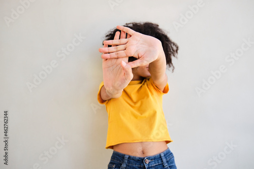 Woman showing stop gesture while standing against white wall photo