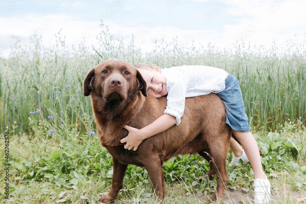 Smiling boy embracing Chocolate Labrador while standing against plants Smiling boy embracing Chocolate Labrador while standing against plants