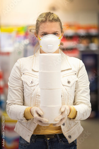 Teenage girl wearing protectice mask and gloves holding stack of four toilet rolls at supermarket photo