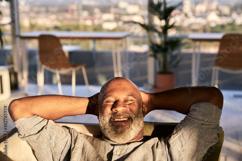 Smiling mature man relaxing on sofa at building terrace during sunset photo