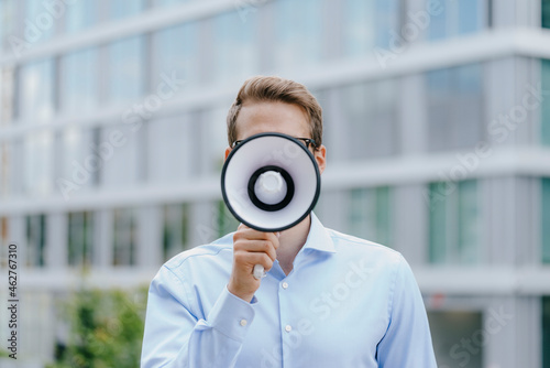 Young businessman standing in front of modern office building, using megaphone photo