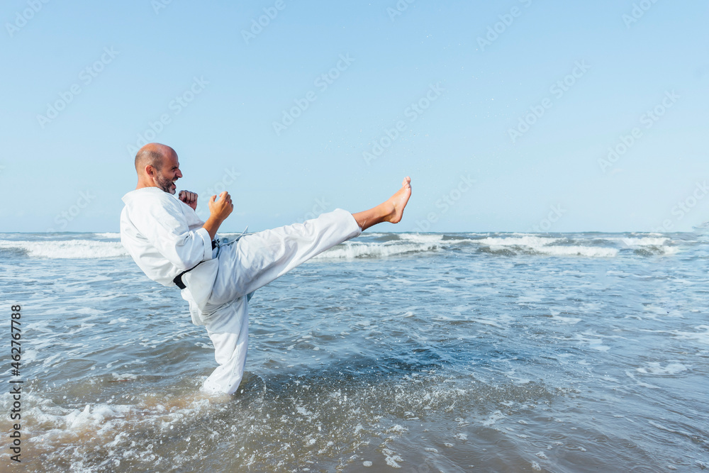 Mature man kicking while practicing karate in sea against clear sky Mature man kicking while practicing karate in sea against clear sky
