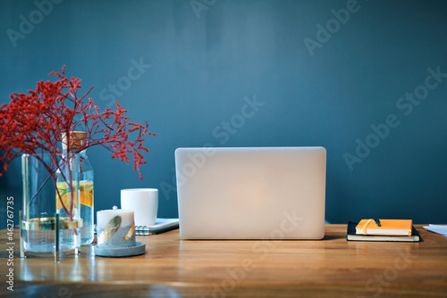 Laptop with diaries and decorations on desk against blue wall in home office photo