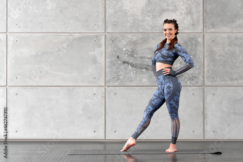 Beautiful sports fitness girl with pigtails posing smiling against the background of a gray stone wall. Camouflage blue tracksuit. Free space for text. Sport and health © Granmedia