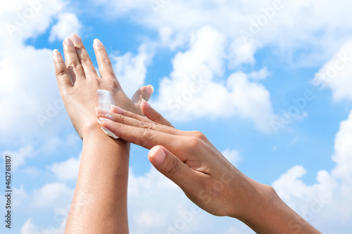 Hand of female holding sunscreen. Very sun light Sky background.Health concepts and skin care