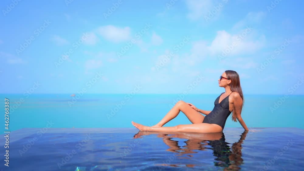 Woman relaxing on the border of rooftop infinity pool with endless seascape on cloudy sky background daytime Woman relaxing on the border of rooftop infinity pool with endless seascape on cloudy sky background daytime