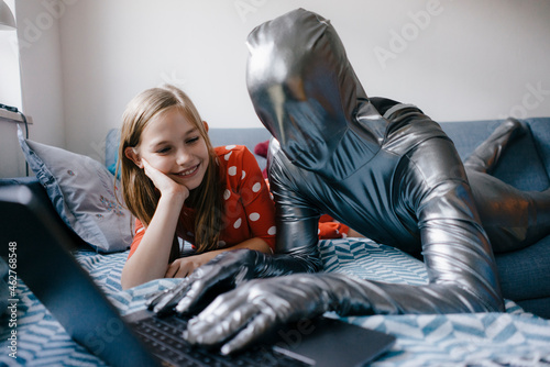 Man in morphsuit and girl lying on couch at home using laptop
