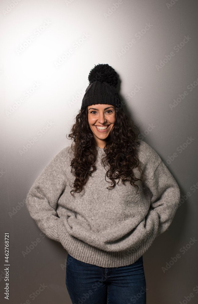 Smiling young woman in knit hat standing against gray wall Smiling young woman in knit hat standing against gray wall