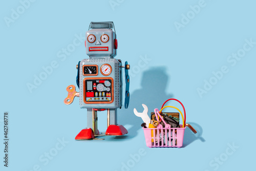 Studio shot of vintage robot toy standing by miniature shopping basket filled with electronic equipment photo
