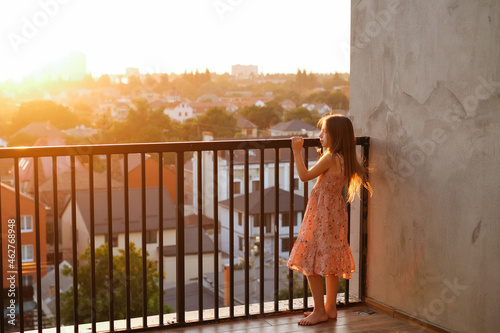 Portrait of a schoolgirl girl in a beautiful pink dress with long hair on a large terrace in the setting sun