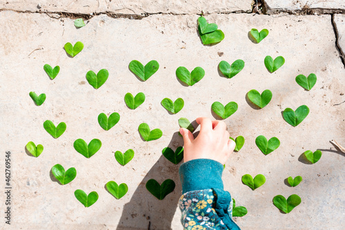 Girl arranging heart shaped green leaves pattern on cement photo