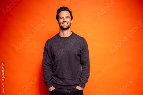 Happy handsome man with hands in pockets against orange background photo