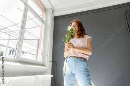 Redheaded woman smelling white peony