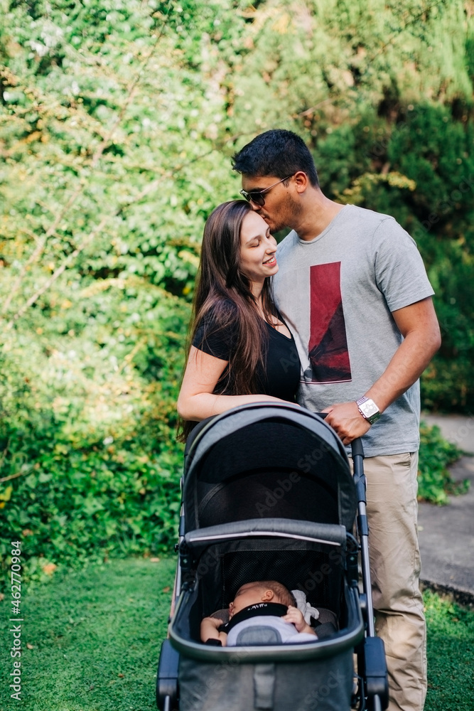 Young man kissing woman while standing with baby carriage at park Young man kissing woman while standing with baby carriage at park