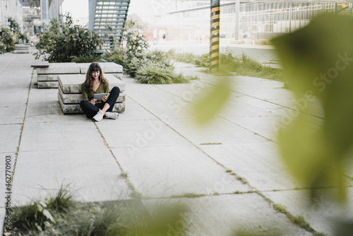 Young smiling woman sitting on the ground and using tablet photo