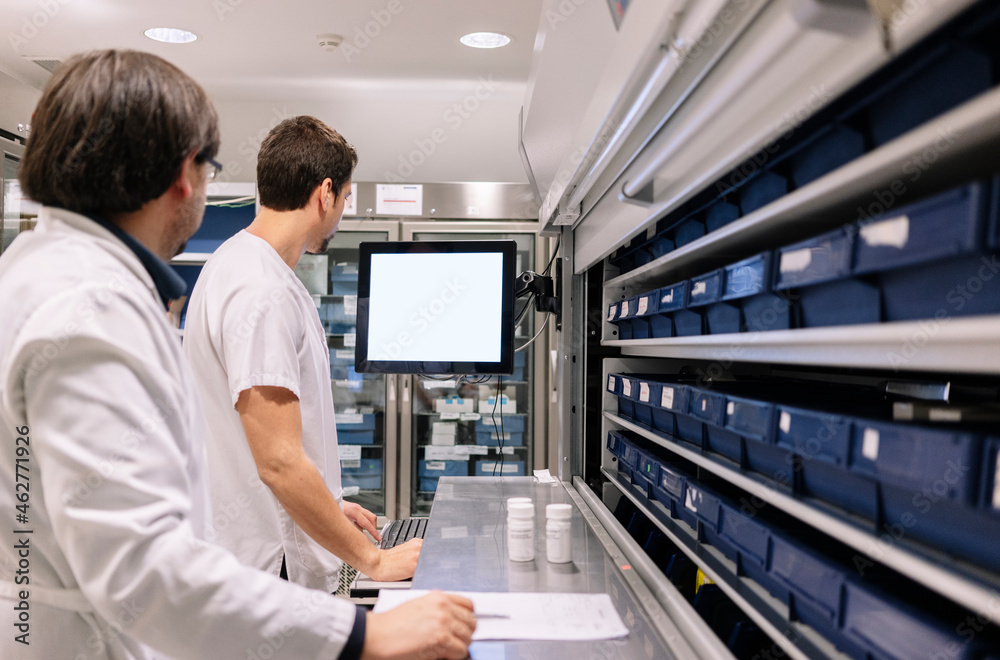 Male doctors using computer while standing in pharmacy at hospital Male doctors using computer while standing in pharmacy at hospital