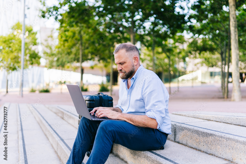 Mature businessman working on laptop while sitting on staircase Mature businessman working on laptop while sitting on staircase