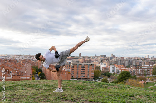 Male acrobat practicing kickboxing against cloudy sky over city photo