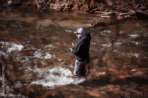Fly fisherman casting in rapid flowing river at forest