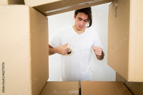 Young man holding adhesive tape by boxes photo