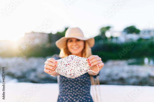 Female tourist holding face mask while standing against clear sky in Binibeca village, Minorca, Spain photo