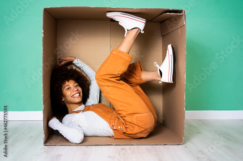 Cheerful woman lying in cardboard box against green wall in new loft apartment photo