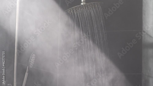 Running hot water streams make vapor in sunlight ray in grey tiled bath cabin equipped with deluxe thermostatic shower system