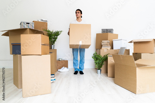 Young man holding big cardboard box while looking away in new house photo
