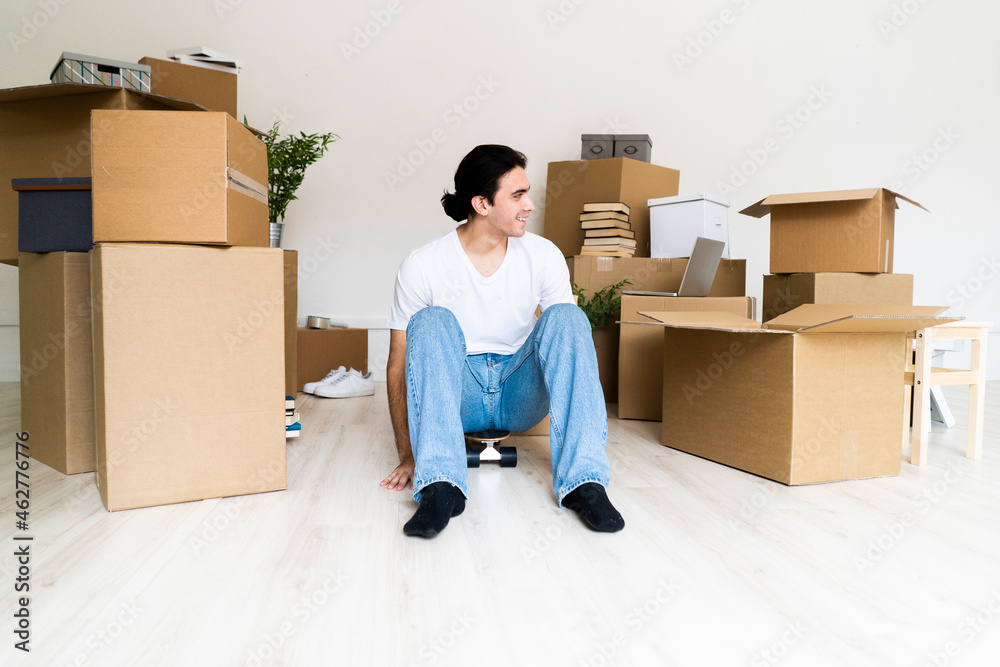 Playful young man sitting on skateboard at new apartment Playful young man sitting on skateboard at new apartment